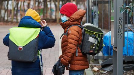 Ein Junge setzt vor dem Schultor seine medizinisch Maske auf, ein anderer sieht ihm dabei zu.