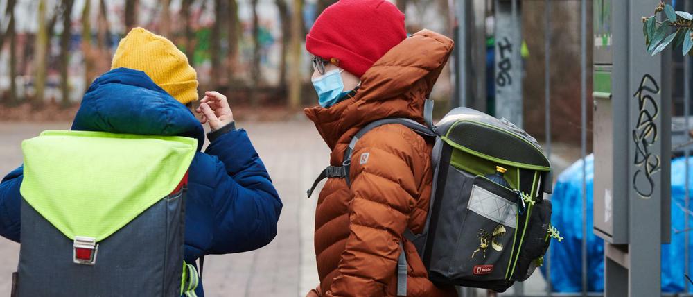 Ein Junge setzt vor dem Schultor seine medizinisch Maske auf, ein anderer sieht ihm dabei zu.