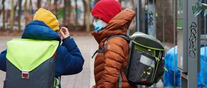 Ein Junge setzt vor dem Schultor seine medizinisch Maske auf, ein anderer sieht ihm dabei zu.