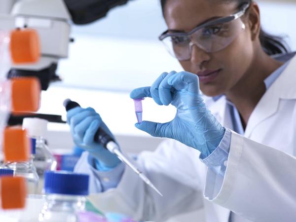 Eine Wissenschaftlerin arbeitet mit Schutzmaske und Handschulen in einem Genetik-Labor.