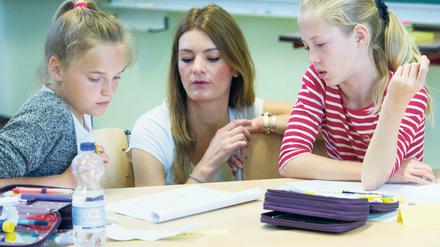 Eine Lehramtsstudentin bespricht mit zwei Viertklässlerinnen ihre Aufgaben.