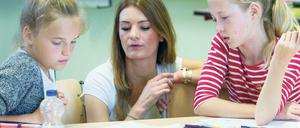 Eine Lehramtsstudentin bespricht mit zwei Viertklässlerinnen ihre Aufgaben.