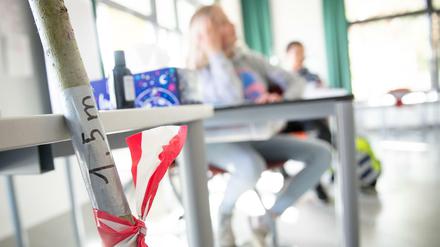 In einem Klassenzimmer wird der Abstand zwischen den Tischen mit einer Stange und Flatterband markiert.