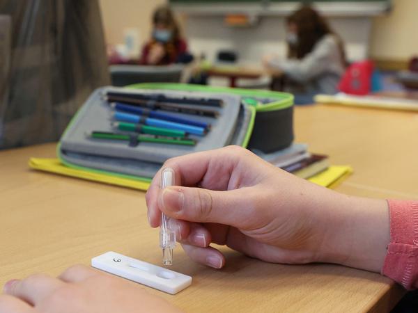 Eine Schülerin sitzt an ihrem Platz im Klassenzimmer und träufelt ihr Sekret in einen Schnelltest.