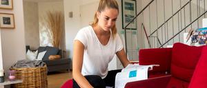 Eine Studentin sitzt mit ihrem Laptop und Lehrbüchern auf dem Sofa.
