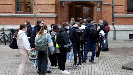 Jugendliche Schüler und Schülerinnen, die Mund-Nasen-Schutz tragen, warten vor ihrem Schulgebäude auf Einlass.