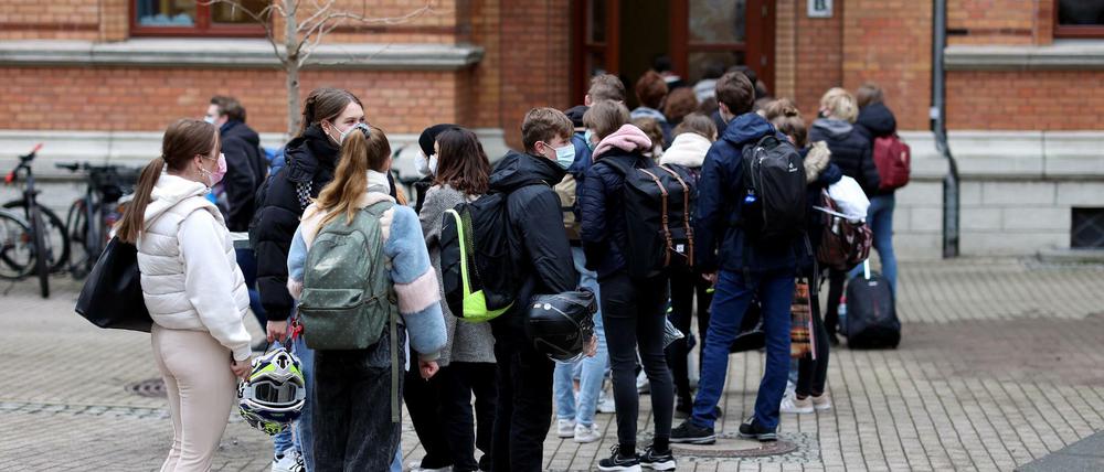 Jugendliche Schüler und Schülerinnen, die Mund-Nasen-Schutz tragen, warten vor ihrem Schulgebäude auf Einlass.