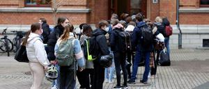 Jugendliche Schüler und Schülerinnen, die Mund-Nasen-Schutz tragen, warten vor ihrem Schulgebäude auf Einlass.