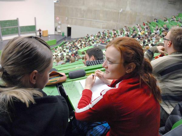 Studierende in einem Hörsaal, im Vordergrund sind zwei Studentinnen im Gespräch zu sehen.