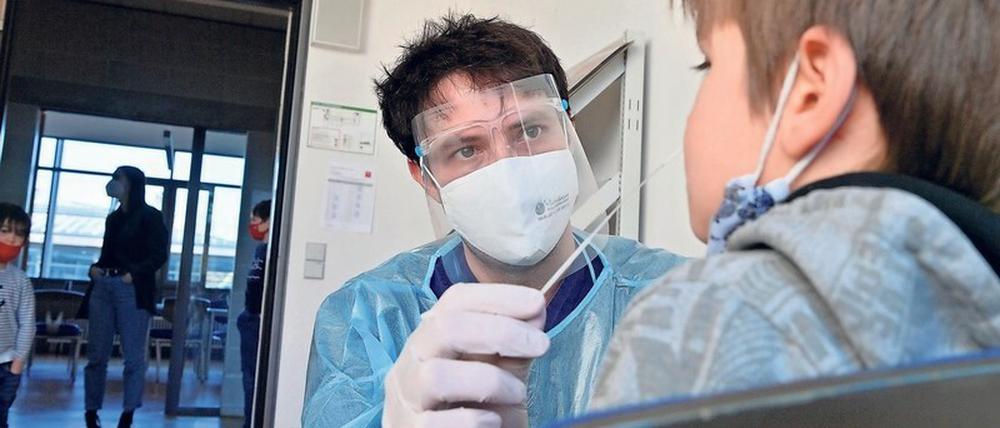Ein junger Mann mit Schutzmaske und Schutzkleidung nimmt einem Schüler für einen Coronatest aus der Nase eine Probe ab.