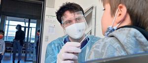 Ein junger Mann mit Schutzmaske und Schutzkleidung nimmt einem Schüler für einen Coronatest aus der Nase eine Probe ab.