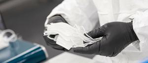 Ein Mitarbeiter eines Unternehmens prüft und stapelt in einem Werk zuvor gefertigte medizinische Masken.