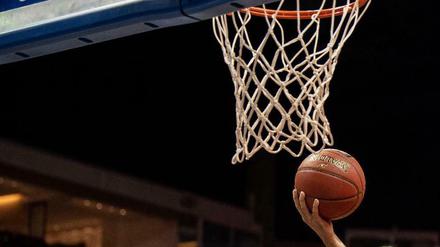 Hand mit Basketball unter Basketballkorb.