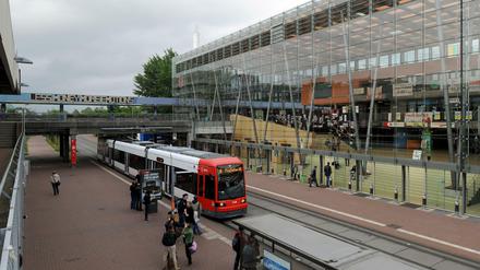 Eine Tramhaltestelle vor dem gläsernen Foyergebäude der Universität Bremen, Studierende warten auf dem Bahnsteig, andere gehen ins Unigebäude.