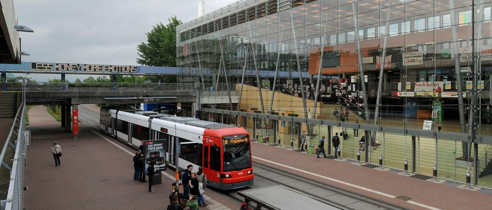 Eine Tramhaltestelle vor dem gläsernen Foyergebäude der Universität Bremen, Studierende warten auf dem Bahnsteig, andere gehen ins Unigebäude.