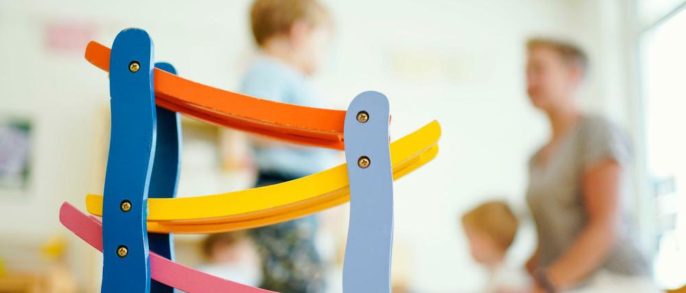 Nur noch Notbetrieb vorgesehen: Eine Erzieherin spielt in einer Kindertagesstätte hinter einer Rollbahn mit Kindern.