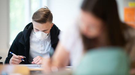 Ein Schüler und eine Schülerin in einer Abiturklasse arbeiten konzentriert im Klassenzimmer, der junge Mann mit Maske.
