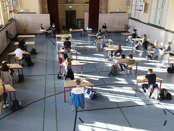Schülerinnen und Schüler sitzen in einer Turnhalle an Einzeltischen .