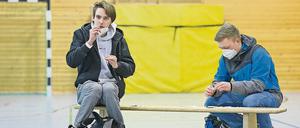 Zwei Oberschüler sitzen in einer Turnhalle und nehmen einen Corona-Sebsttest an sich vor.