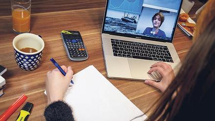 Eine Studentin arbeitet zu Hause an ihrem Schreibtisch, auf dem Laptop läuft eine Videokonferenz.