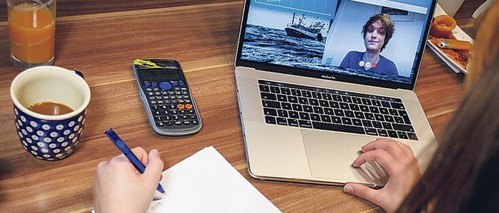 Eine Studentin arbeitet zu Hause an ihrem Schreibtisch, auf dem Laptop läuft eine Videokonferenz.