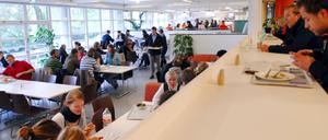 Studierende sitzen in einer Mensa, essen und unterhalten sich.