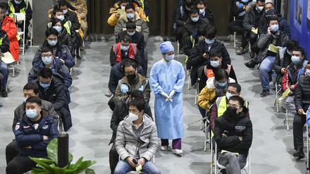 Eine Medizinerin geht zwischen Menschen entlang, die in Peking gerade eine Impfdosis mit einem Corona-Impfstoff erhalten haben.
