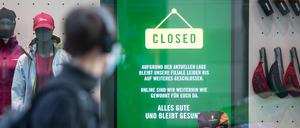 Bekleidungsgeschäft mit Hinweis auf pandemiebedingte Schließung und Onlinehandel, davor Passant mit Coronamaske.