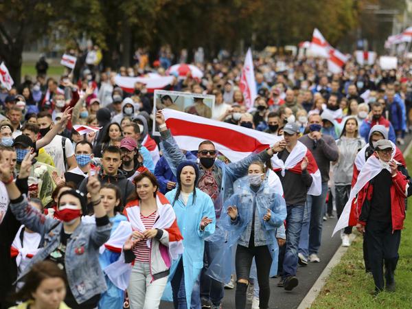 Demonstrierende laufen in dichten Reihen durch eine breite Straße und tragen rot-weiße Flaggen.