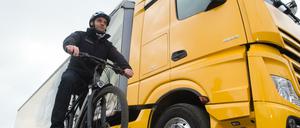 Größenunterschied: Ein Radfahrer steht mit seinem Fahrrad in der Versuchsabteilung von Mercedes Benz neben einem Lkw.