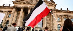 Teilnehmer einer Kundgebung gegen die Corona-Maßnahmen stehen vor dem Reichstag, ein Teilnehmer hält eine Reichsflagge.