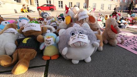 Kuscheltieren, die auf einem öffentlichen Platz ausgelegt wurden, haben Protestierende Klebeschilder mit Texten wie "Keine Masken für Kinder" und "Keine Luft" auf die Schnauzen geklebt.