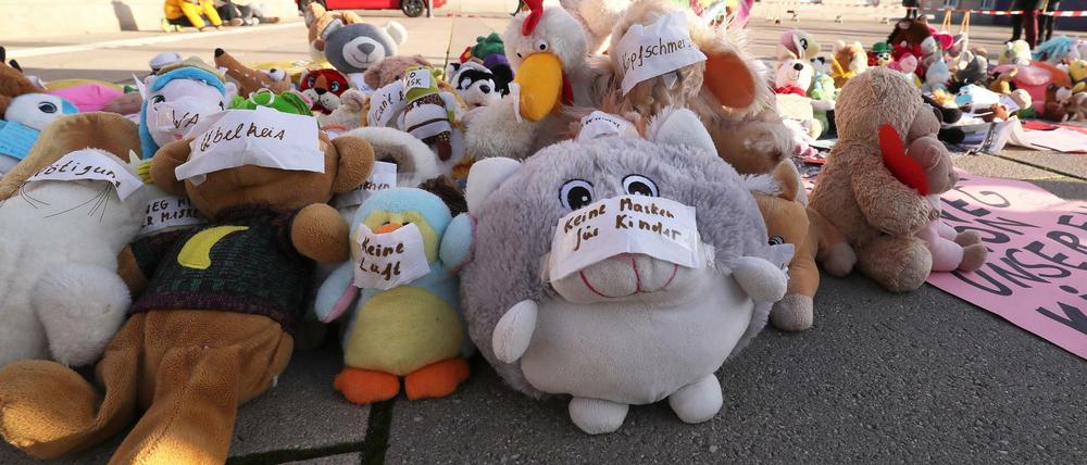 Kuscheltieren, die auf einem öffentlichen Platz ausgelegt wurden, haben Protestierende Klebeschilder mit Texten wie "Keine Masken für Kinder" und "Keine Luft" auf die Schnauzen geklebt.