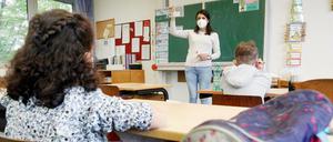 Eine Grundschullehrerin seht vor ihrer Klasse und erklärt einen Corona-Selbsttest.