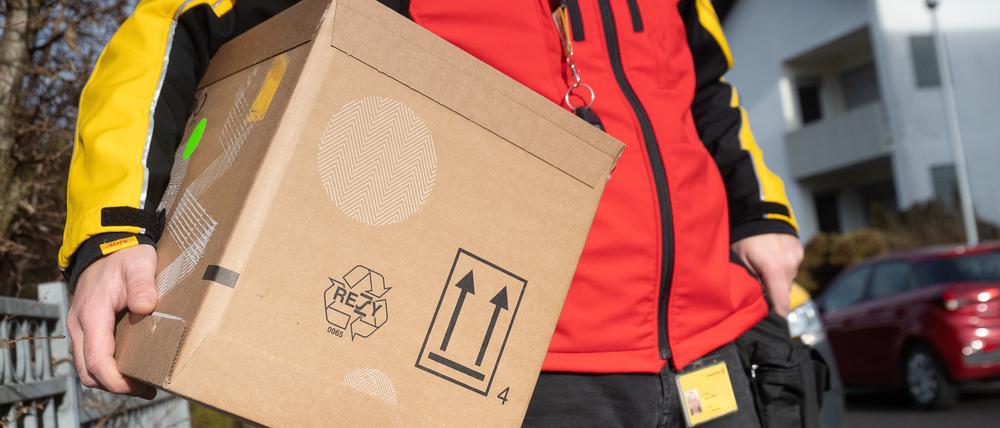Ein DHL-Mitarbeiter trägt ein Paket unter seinem Arm.