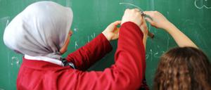 Eine Lehrerin hilft einer Schülerin an der Tafel beim Einsatz des Zirkels.