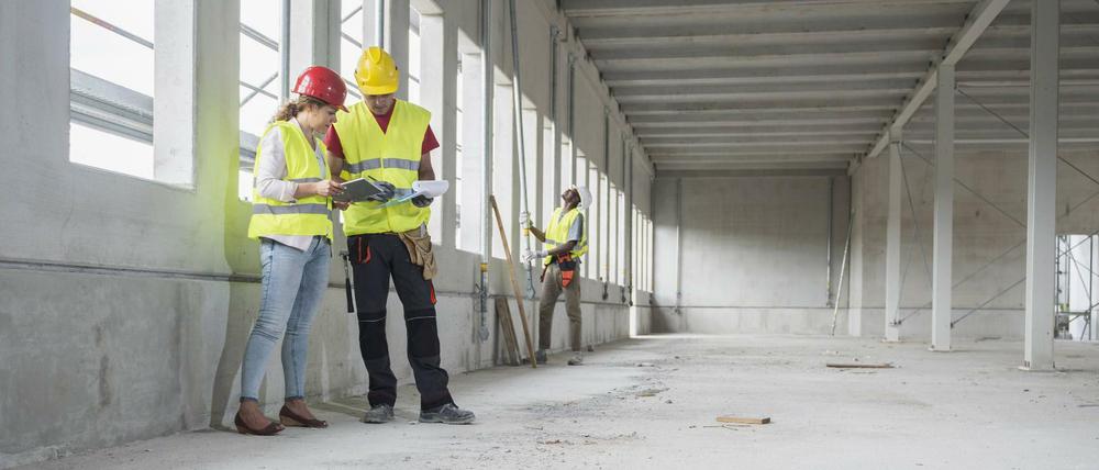 Eine Architektin bespricht sich mit einem Arbeiter auf einer Baustelle.