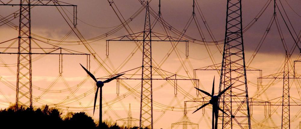 Strommasten und Windräder heben sich wie Scherenschnitte vom farbenprächtigen Abendhimmel ab.