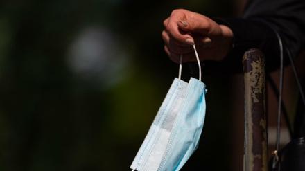 Ein Frau hält vor einem Bäckereigeschäft ihren Mundschutz in der Hand. 