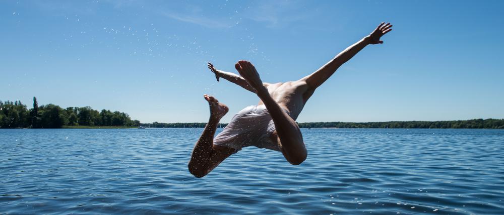 Ein Mann springt von einer Uferkante ins Wasser. 