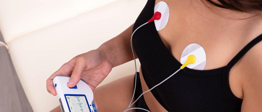 Eine junge Frau überwacht mit Elektroden und Monitor ihren Herzschlag.