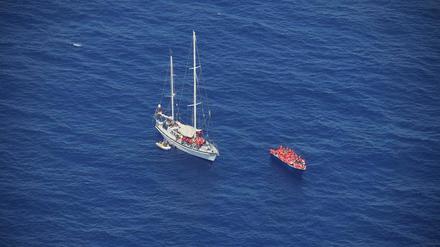 Migranten sitzen mit Rettungswesten in einem Holzboot und auf dem von einem deutschen Verein betriebene Hilfsschiff Nadir.