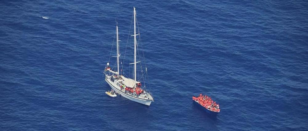 Migranten sitzen mit Rettungswesten in einem Holzboot und auf dem von einem deutschen Verein betriebene Hilfsschiff Nadir.