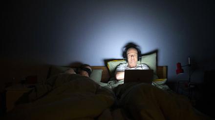 Ein Mann liegt mit seinem Laptop im Bett. 