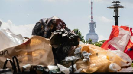 Der Berliner Fernsehturm ragt hinter einem vollen Mülleimer im Volkspark Friedrichshain hervor. 
