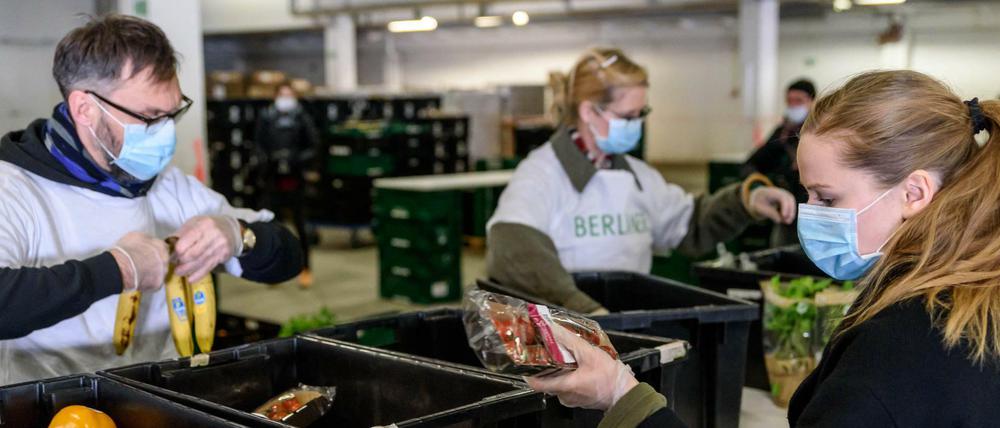Ehrenamtliche Helfer der Berliner Tafel packen mit Atemschutzmasken Lebensmittel in Tüten.