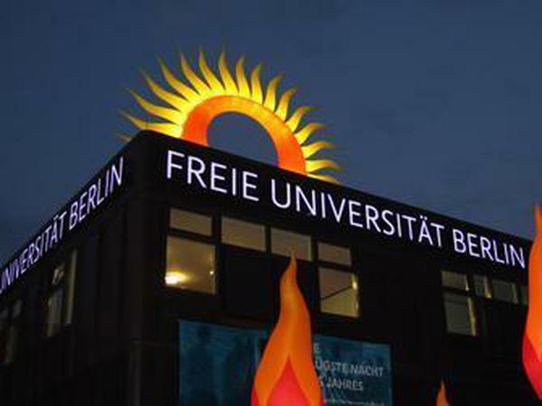 Über einem Hauptgebäude der FU leuchtet eine Sonne und vor dem Gebäude flattern künstliche Feuer.