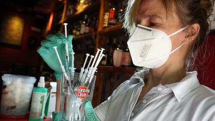 Eine medizinische Fachangestellte sortiert in der Revolte-Bar im Berliner Bezirk Friedrichshain Spritzen mit dem Impfstoff Johnson &amp; Johnson in einem Glas.