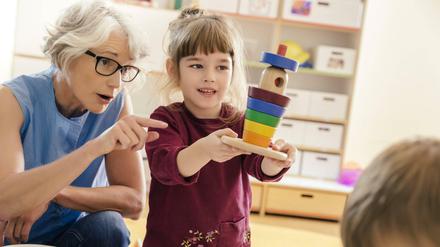 Eine Kitaerzieherin im Gespräch mit einem Mädchen im Vorschulalter.