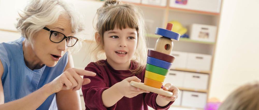 Eine Kitaerzieherin im Gespräch mit einem Mädchen im Vorschulalter.